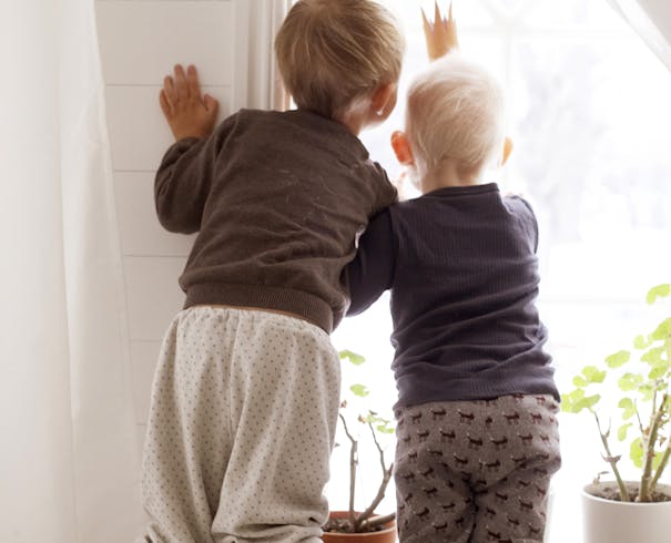 Två små barn tittar ut genom ett fönster
