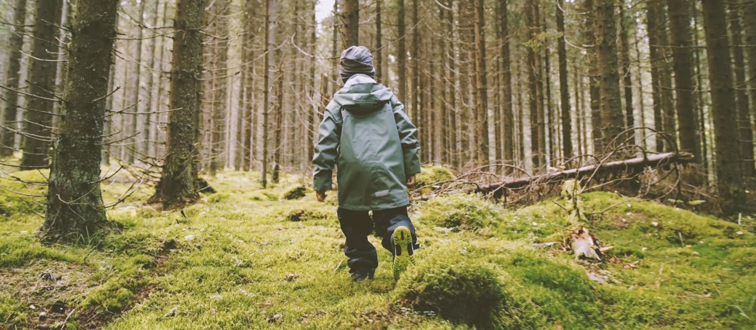 Barn i regnkläder springer i skogen
